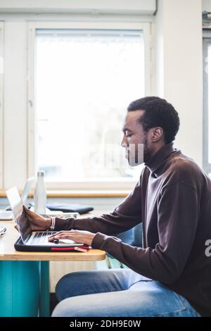 Side view of male student using laptop at table in university cafeteria Stock Photo