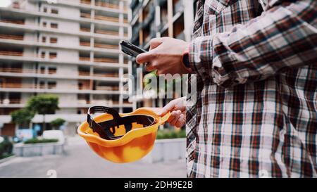 Young Engineer using smartphone on construction site. Architect using phone. Manager development building texting on smart phone Stock Photo