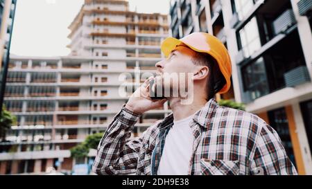 Portrait of young handyman making call while standing at construction area. Engineer talking on the phone on a construction site Stock Photo