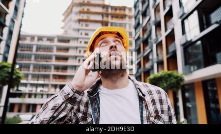 Portrait of young handyman making call while standing at construction area. Engineer talking on the phone on a construction site Stock Photo