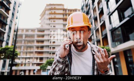 Engineer talking on phone. Architect using phone on construction site. Foreman phone call control process. Construction worker c Stock Photo