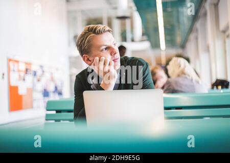 Thoughtful young male student sitting in cafeteria at university Stock Photo