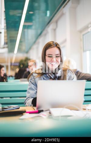 Smiling female student using laptop in cafeteria Stock Photo