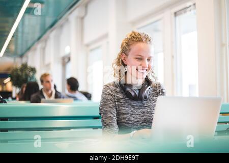 Smiling young female student using laptop in cafeteria Stock Photo