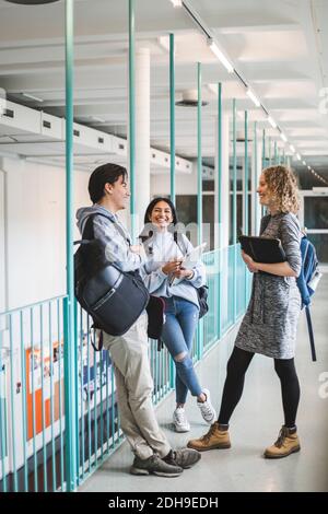 Male and female students talking while standing in corridor of university Stock Photo