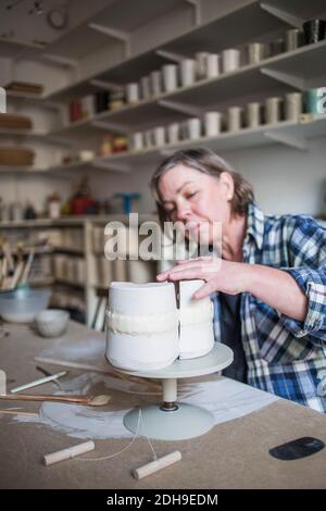Mature female potter working at vase on table in workshop Stock Photo