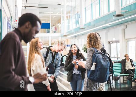 Cheerful young male and female students talking while standing in cafeteria at university Stock Photo