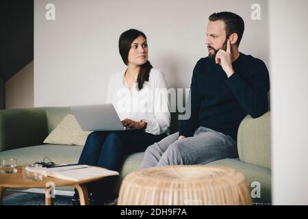 Business colleagues discussing while sitting on sofa at office lobby Stock Photo