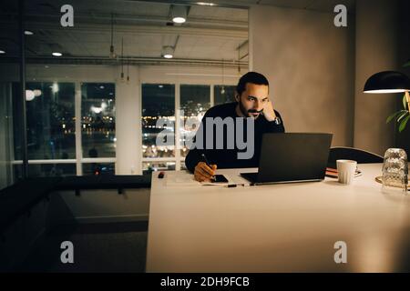 Tired businessman working late while sitting at desk in illuminated creative office Stock Photo