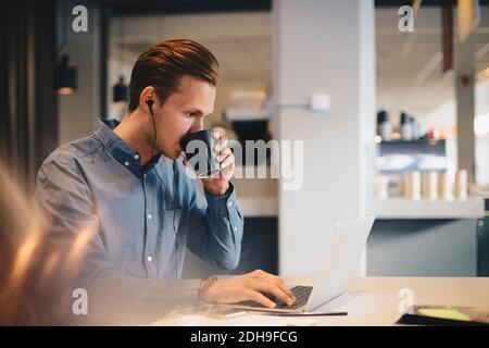 Businessman drinking coffee while using laptop at desk in office Stock Photo