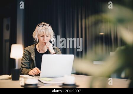 Thoughtful businesswoman using laptop at desk in office Stock Photo