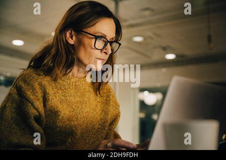 Determined mature female entrepreneur working late while using laptop at workplace Stock Photo
