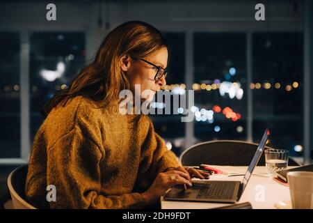 Ambitious businesswoman using laptop while working late at creative office Stock Photo