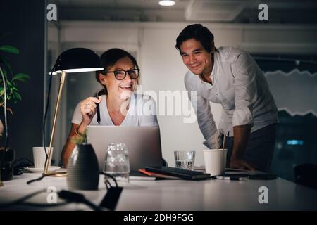 Happy mature businesswoman working late while planning strategy with colleague at creative workplace Stock Photo