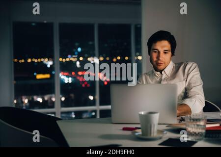 Confident businessman using laptop while sitting at desk in creative workplace Stock Photo