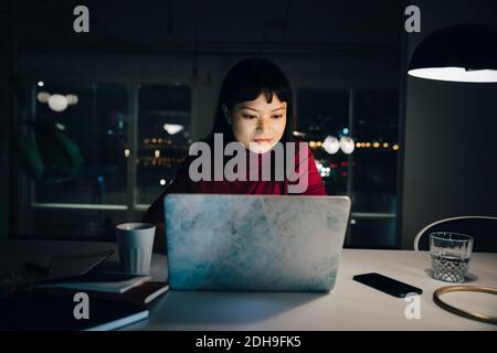 Confident young female professional using laptop while working late in creative workplace Stock Photo