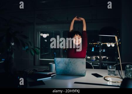 Smiling young businesswoman stretching while working late in coworking space Stock Photo