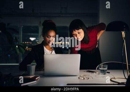 Confident female business colleagues discussing over laptop while working late at creative office Stock Photo