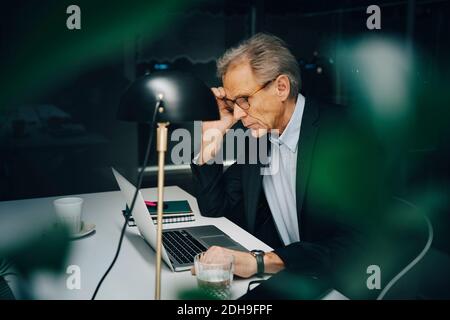 Worried senior businessman working late while sitting with laptop at coworking space Stock Photo