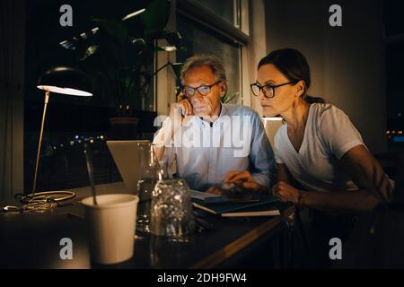 Businesswoman with senior businessman planning strategy in dark office while working late Stock Photo