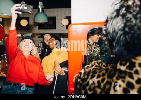 Smiling female taking selfie with friends in cafe Stock Photo