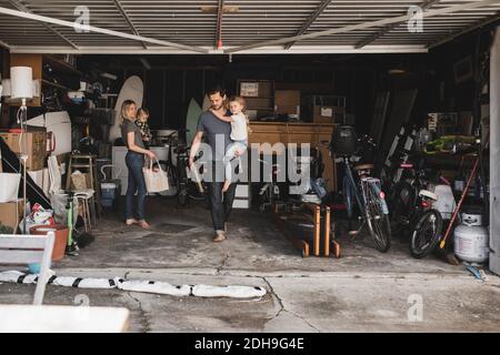 Mid adult parents carrying children while working in storage room at garage Stock Photo