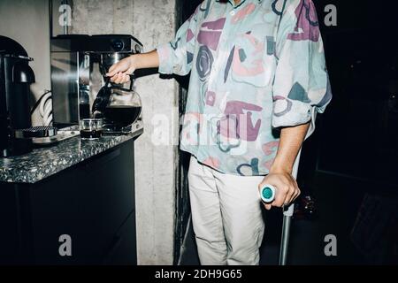 Midsection of young man with crutch making coffee at workplace Stock Photo
