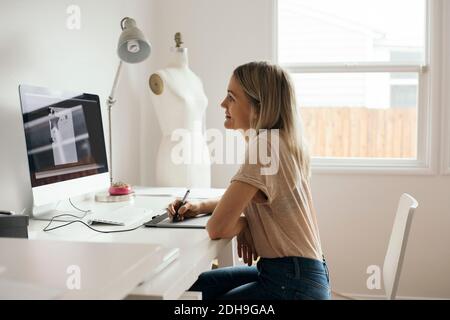 Side view of creative female designer using graphics tablet at home Stock Photo