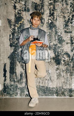 Portrait of businessman with coffee standing against wall in workplace Stock Photo