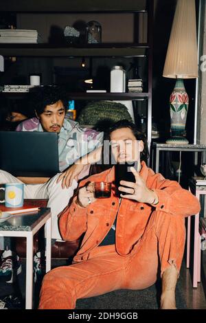 Male entrepreneur showing smart phone to coworker while drinking coffee in creative office Stock Photo