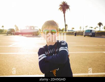 Portrait of confident boy wearing sunglasses while standing arms crossed at parking lot on sunny day Stock Photo