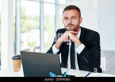Confident young businessman in elegant suit posing in a bright modern office. sitting at his desk Stock Photo