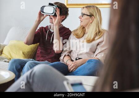 Mother looking at son using virtual reality headset while sitting on sofa Stock Photo