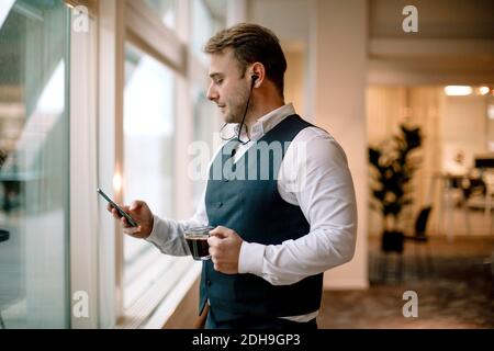 Businessman wearing headphones using mobile phone while having coffee at office Stock Photo
