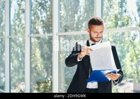 Confident handsome businessman with clipboard working on documents in a bright modern office with copy space Stock Photo