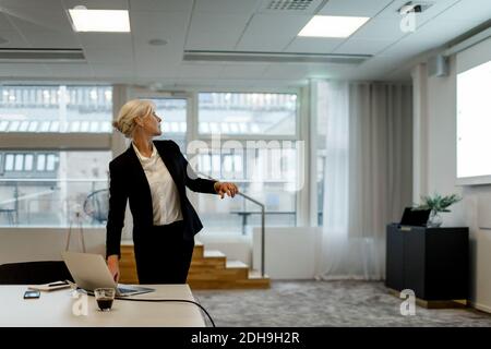 Confident businesswoman using laptop while looking at flat screen in board room Stock Photo