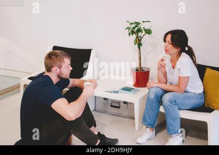Creative business colleagues holding coffee cups while talking at office lobby Stock Photo