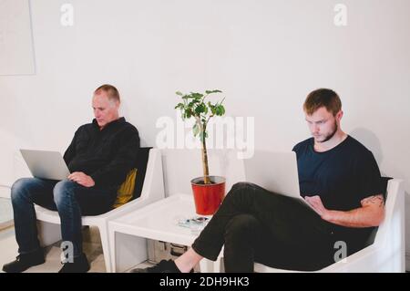 Businessmen using laptops while sitting at lobby in creative office Stock Photo