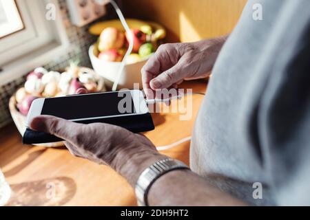 Cropped image of senior man connecting cable to mobile phone at kitchen counter Stock Photo