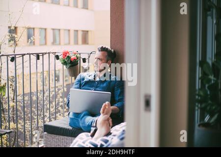 Man sitting on balcony with laptop looking out Stock Photo