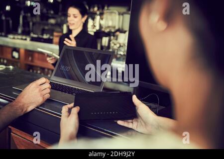 Cropped hand of man using laptop while woman holding modem in cafe Stock Photo