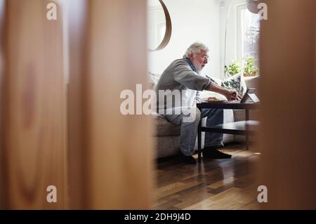Senior man using digital tablet while having breakfast seen through wooden columns Stock Photo