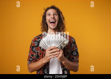 Image of excited young handsome man posing with dollars isolated over yellow background Stock Photo