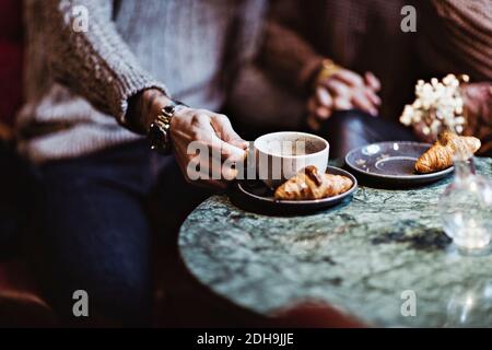 Midsection of man holding coffee while sitting with female partner in hotel Stock Photo
