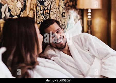 Happy mid adult man talking with girlfriend while relaxing on bed in hotel room Stock Photo