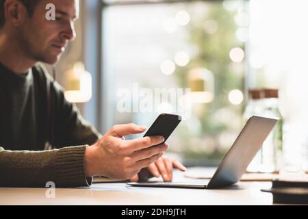 Serious businessman using mobile phone while using laptop at table in office Stock Photo