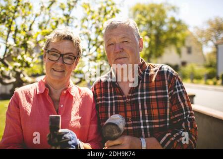 Portrait of confident senior couple holding hammers while standing at yard Stock Photo