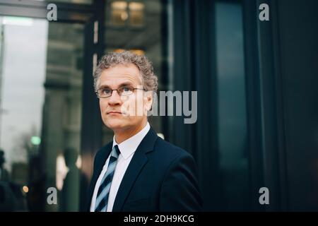 Male businessman wearing suit looking away while standing in city Stock Photo