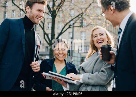 Happy business coworkers with book discussing while standing in city Stock Photo