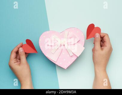 Hands holding a pink cardboard box with a bow on a blue background Stock Photo